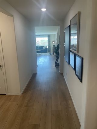 A bright hallway with wood floors, modern lighting, and framed art leads to a cozy living area.