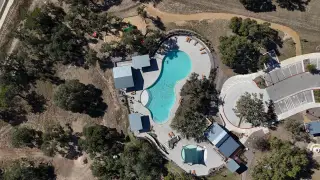 A bird's-eye view of the Caliterra community by Drees Custom Homes in Dripping Springs, TX, featuring a uniquely shaped pool, playground, and winding paths, surrounded by natural beauty.