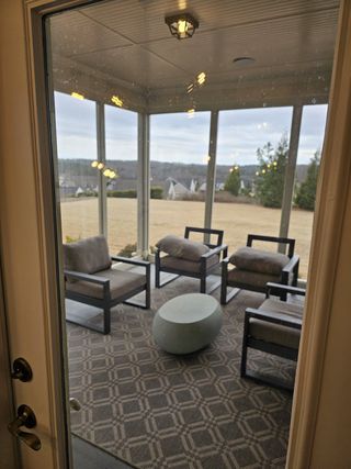 A cozy sunroom with modern seating, geometric rug, and scenic views, perfect for relaxation.