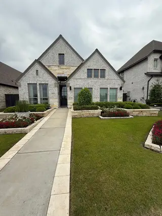 A charming light brick home with peaked roofs and manicured landscaping in Harvest Green 45' by Perry Homes (Richmond, TX).