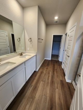 A stylish bathroom featuring dual sinks, white cabinetry, and wood-look flooring leading to a walk-in closet.