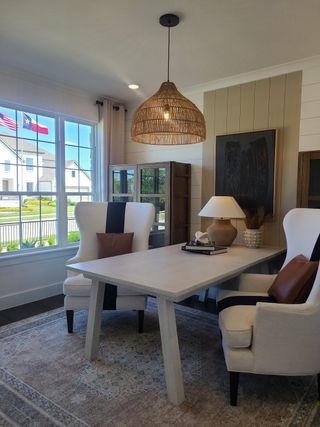 Model Home A cozy office with modern chairs, a sleek table, and a woven pendant light, featuring a large window view.