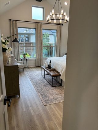 Model Home A cozy bedroom with wood floors, elegant chandelier, large window, and chic decor.