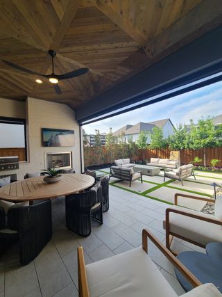 A chic outdoor living space with cozy seating, a round dining table, fireplace, and lush garden views.