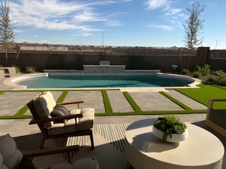 Model Home A modern backyard with a sleek pool, stylish patio seating, and lush greenery under a clear blue sky.