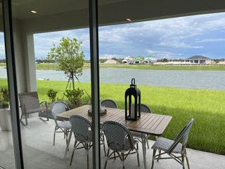 Model Home A serene patio with a stylish dining set overlooks a picturesque lake, with lush greenery and vibrant surroundings.