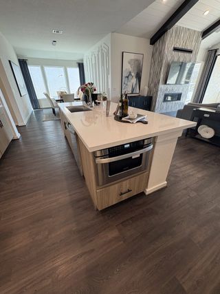 Model Home An open-concept kitchen with a waterfall island, integrated microwave, and dark wood flooring in Esperanza by Scott Felder Homes (Boerne, TX).