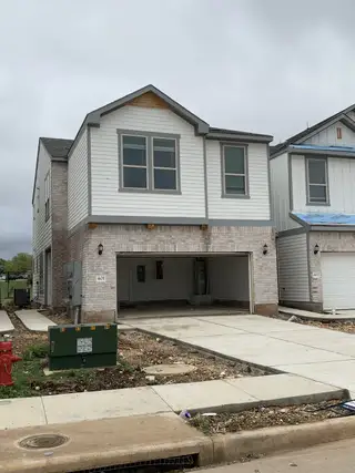 Street view A newly built townhome in Whitestone Preserve by Pulte Homes (Cedar Park, TX) with a sleek garage door, white siding, and brick accents.