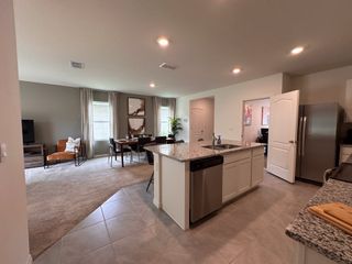 Open-concept living area with granite kitchen island, cozy seating, and a dining space next to large windows.