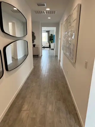 A modern hallway with wood-tiled flooring, sleek mirrors, and contemporary artwork leading to a cozy living room space.