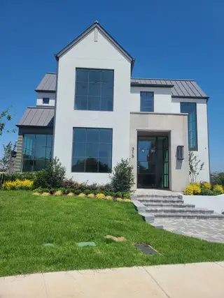 A modern white home with large windows and manicured landscaping in Avadene at Las Colinas by Alexander Hunt Distinct Homes (Irving, TX).