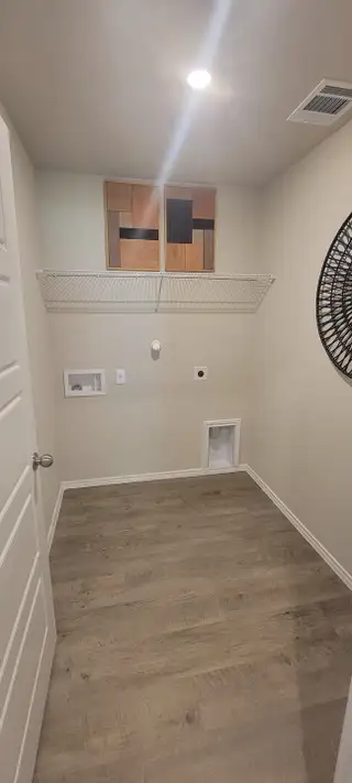A modern laundry room featuring vinyl flooring, an overhead shelf, and decorative wall art.