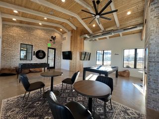 Community Amenities A modern recreational room with foosball, cozy seating, and a large ceiling fan under exposed beams.