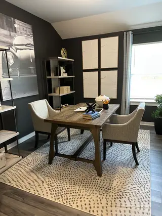 A cozy study with wood flooring, modern furnishings, and natural light through a large window.