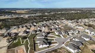 An expansive aerial view of Crescent Bluff by Scott Homes (Georgetown, TX), showcasing a sprawling neighborhood with homes nestled amongst rolling hills and trees.