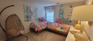 Model Home A whimsical bedroom with twin beds featuring colorful floral bedding, a hanging egg chair, and surf-themed decor, creating a playful space.