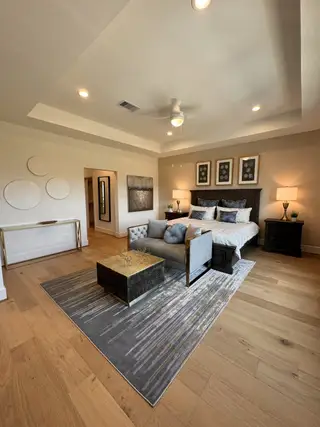 Model Home A spacious bedroom with a sleek gray rug, modern decor, cozy seating, and elegant artwork, creating a serene retreat.
