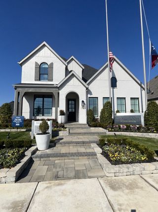 A stunning white brick home with charming shutters and a landscaped yard in The Parks at Wilson Creek by Highland Homes (Celina, TX).