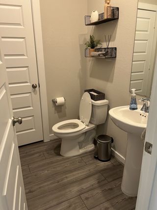 A modern bathroom featuring sleek shelving, a pedestal sink, and elegant wood-style flooring.
