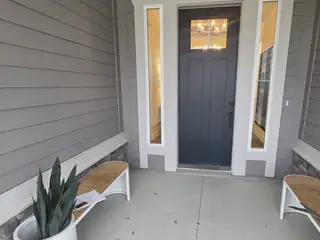 A welcoming entryway with a dark door, sidelights, and modern benches, accented by a potted plant.