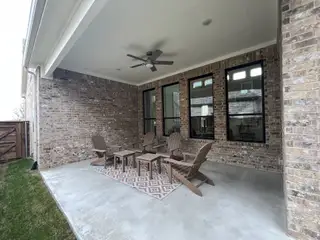 A covered patio with brick walls, outdoor seating, and a ceiling fan in Solterra Texas by Brightland Homes (Mesquite, TX).