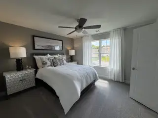 A cozy bedroom with a plush bed, modern lamps, elegant decor, and soft natural light streaming through large windows.