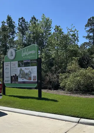 Welcoming sign to Evergreen by Chesmar Homes, surrounded by lush greenery in Conroe, TX.