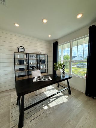 A bright home office with shiplap walls, modern black desk, open shelving, and large window for natural light.