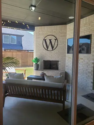 A cozy patio features wicker seating, a fireplace, and stylish decor under a shaded pergola. Ideal for outdoor relaxation.