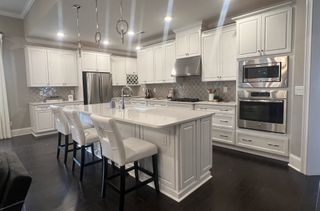 Model Home A sleek kitchen with white cabinetry, marble countertops, pendant lighting, and stainless steel appliances.
