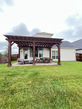 A lovely white brick home with a wooden pergola and lawn in Edgewater by Grand Homes (Fate, TX).