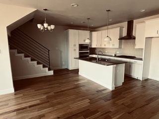 A modern kitchen with sleek cabinetry, island, and pendant lighting, featuring hardwood floors and a stylish staircase.
