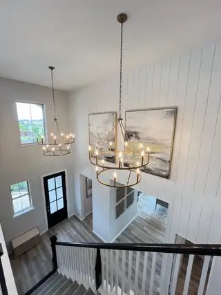 An elegant entryway with dual chandeliers, modern accents, and hardwood floors creates a welcoming and stylish atmosphere.