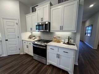 Modern kitchen with white cabinets, stainless steel appliances, and gray tile backsplash. Dark wood flooring adds warmth.