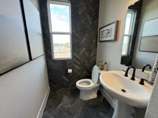 A sleek powder room with a pedestal sink, modern black fixtures, and a herringbone tile accent wall.