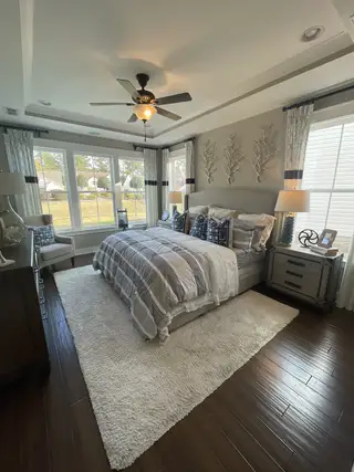 A cozy bedroom with a large window, soft bedding, elegant decor, and rich hardwood floors.