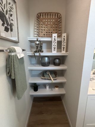 A cozy nook with decorative shelves, featuring art pieces, greenery, and towels, creating a stylish, intimate vibe.