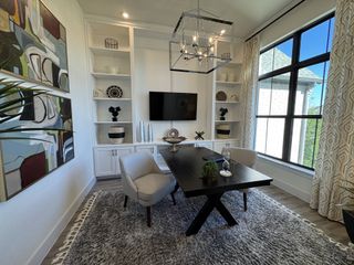 A stylish home office with built-in shelving, a modern chandelier, and large windows for natural light.