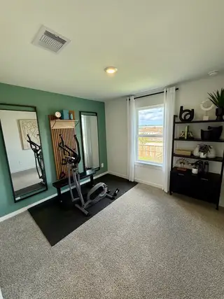 A modern exercise room with a stationary bike, full-length mirrors, and a stylish green accent wall.