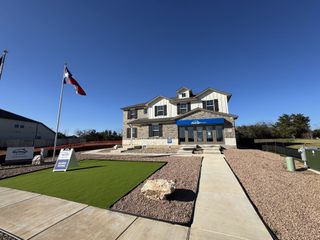A charming two-story model home with a flag, stone accents, and manicured lawn in Opal Meadows by Meritage Homes (Kyle, TX).