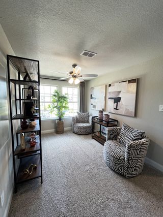 Model Home A cozy room featuring patterned armchairs, stylish shelving, abstract art, and a large window for ample natural light.