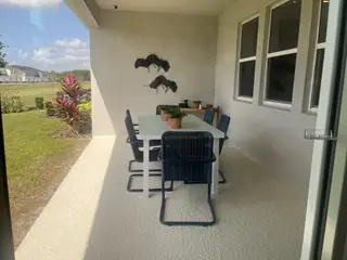 A cozy patio with a sleek white table, blue chairs, and potted plants, perfect for outdoor dining and relaxation.