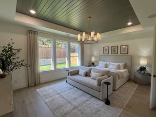 Model Home A spacious bedroom with a plush bed, elegant chandelier, cozy seating, and large windows offering a view of the backyard.