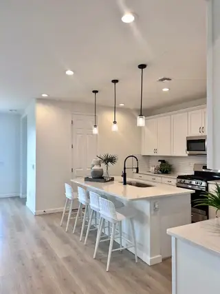 A modern kitchen featuring white cabinetry, a sleek island with seating, pendant lighting, and stainless steel appliances.