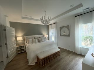 A serene bedroom with a textured accent wall, elegant chandelier, cozy bedding, and soft natural light filtering through sheer curtains.