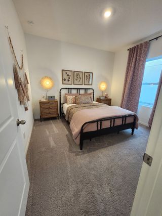 A cozy bedroom featuring a wrought iron bed, soft carpet, and elegant decor with warm lighting and textured drapes.