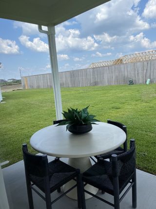A cozy patio with a round table, black woven chairs, and lush green lawn views under a clear blue sky.