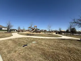 Community Amenities The playground area at Davis Ranch by Pulte Homes (San Antonio, TX) surrounded by walking paths and greenery, perfect for kids to have fun while parents relax nearby.