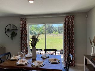 Model Home A cozy dining area with a wooden table set for dinner, featuring large windows and vibrant curtains overlooking a lush backyard.
