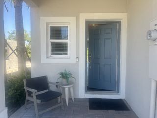 A cozy front porch with a blue door, black chair, and potted plant on a small table.